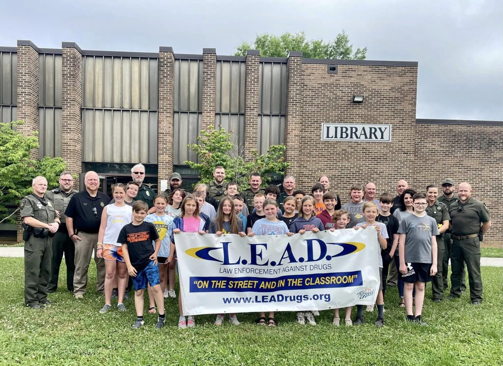 Students and police officers hold a L.E.A.D. Camp banner.